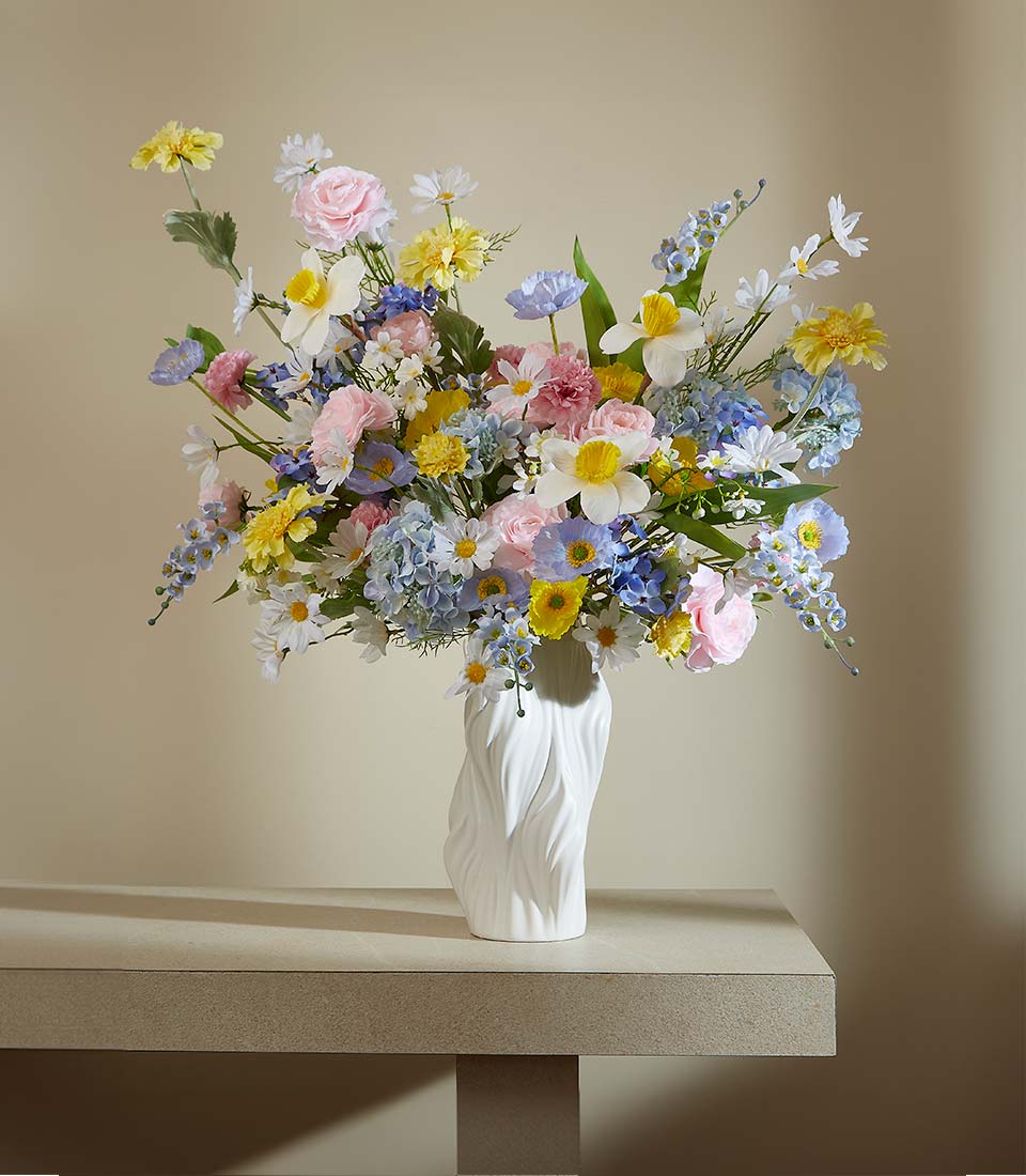 Vibrant pastel artificial flowers in white ceramic vase with pink roses, daffodils, and hydrangeas
