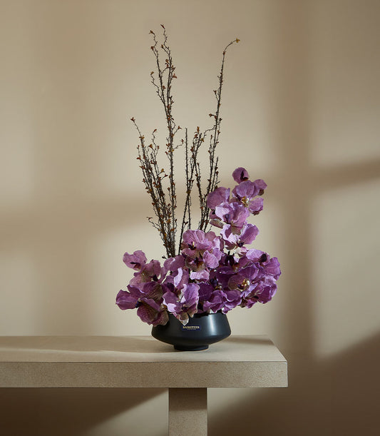 Purple artificial orchid arrangement in matte black ceramic vase with dried branches, premium luxury gift