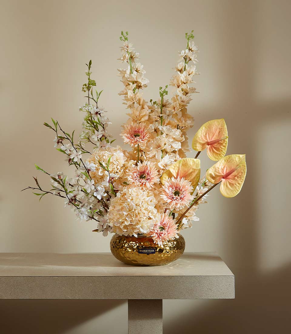 Sophisticated Elegance artificial flower arrangement in gold hammered vase with pink gerberas, white clusters, and tropical