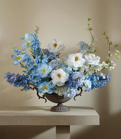 Elegant artificial flower arrangement in blue and white peonies, irises, and hydrangeas in a dark grey ornate urn vase