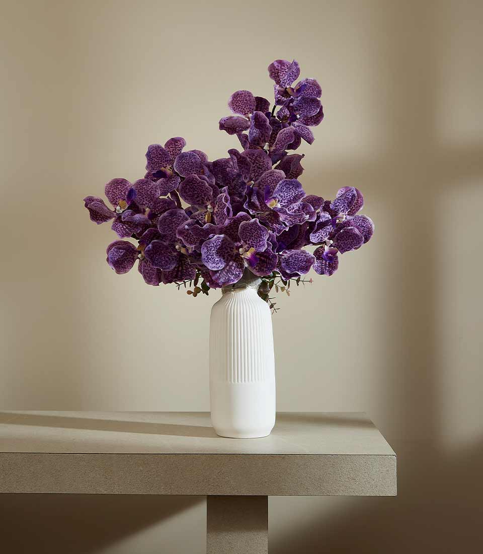 Purple speckled orchids in textured white ceramic vase, modern minimalist arrangement