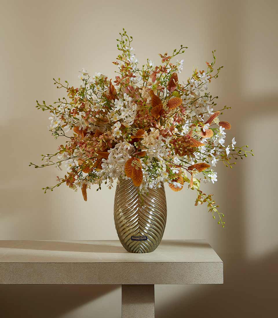 Elegant white and cream artificial flower arrangement in metallic bronze vase with rust-orange accents