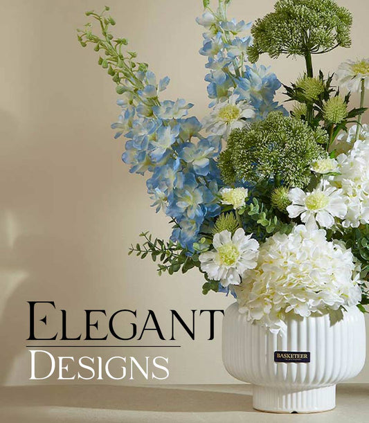 Elegant artificial flower arrangement with blue delphiniums, white hydrangeas, and green foliage in white ribbed ceramic vase
