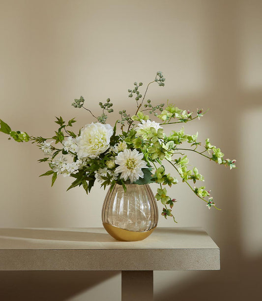 Amber ribbed glass vase with gold base holding white peonies, dahlias, and green foliage artificial flower arrangement