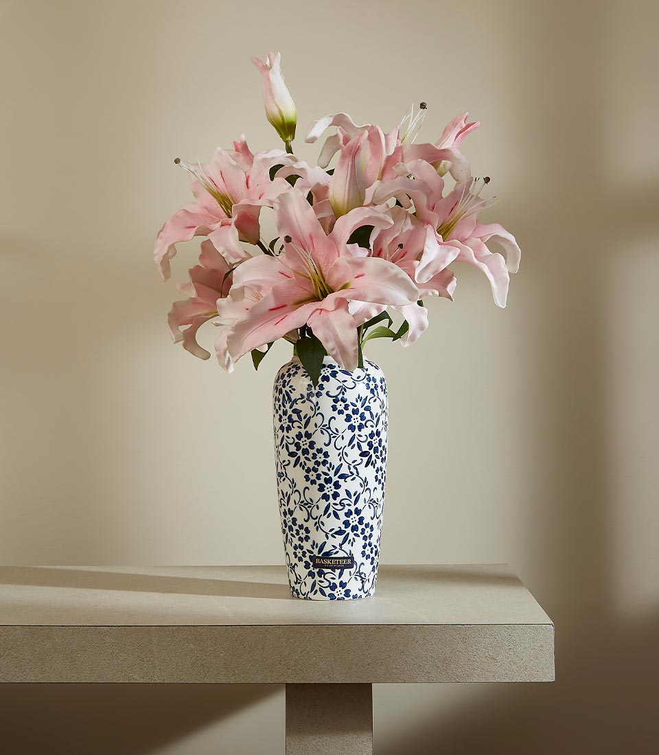 Tall blue and white ceramic vase with light pink artificial lilies and dense floral pattern
