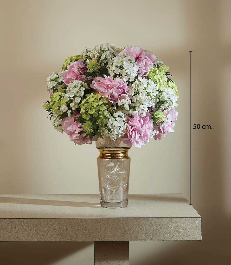 Springtime artificial flower arrangement with pink peonies, white blooms, and green hydrangeas in gold-rimmed glass vase