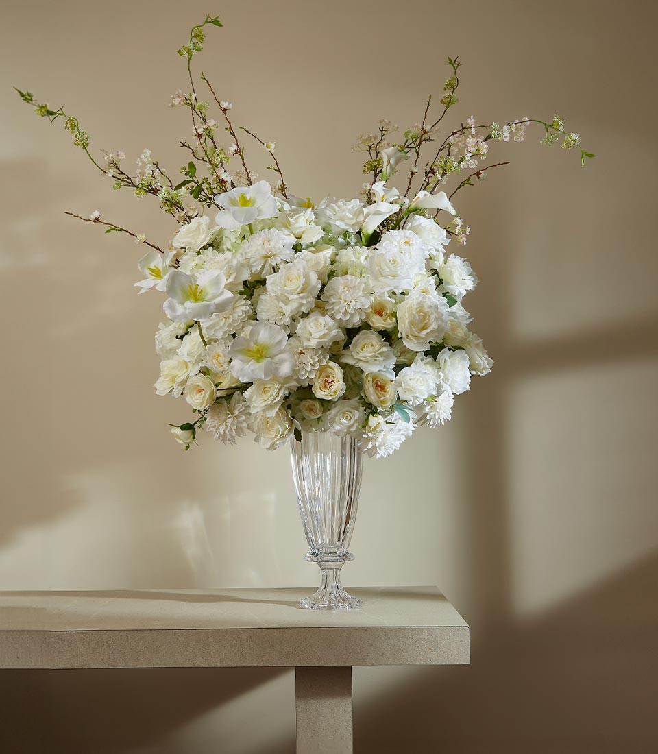 White roses, dahlias, and tulips in tall fluted vase with lush artificial flower arrangement