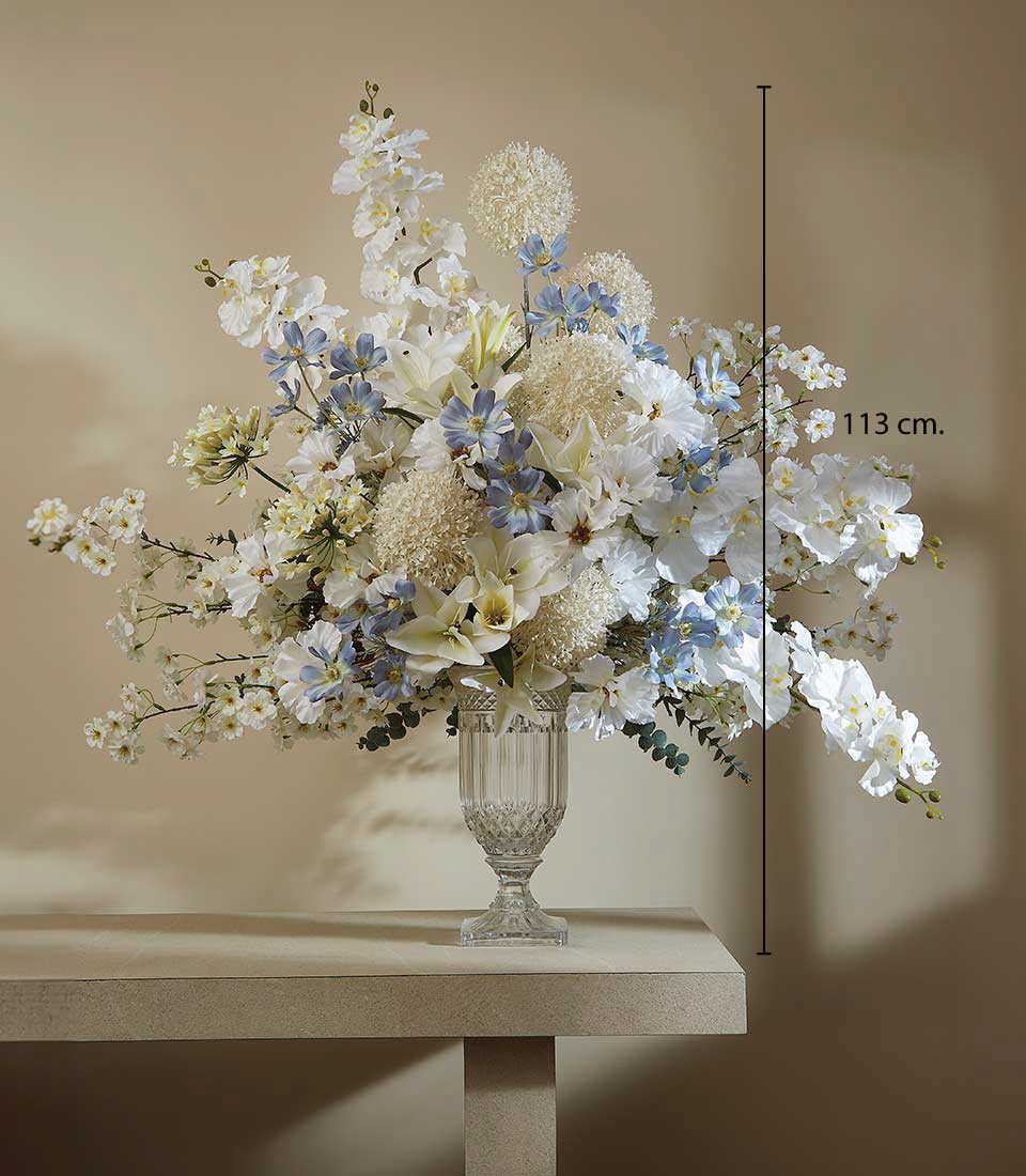 Ethereal white and light blue artificial flower arrangement in cut-glass vase with orchids, lilies, and delicate blooms