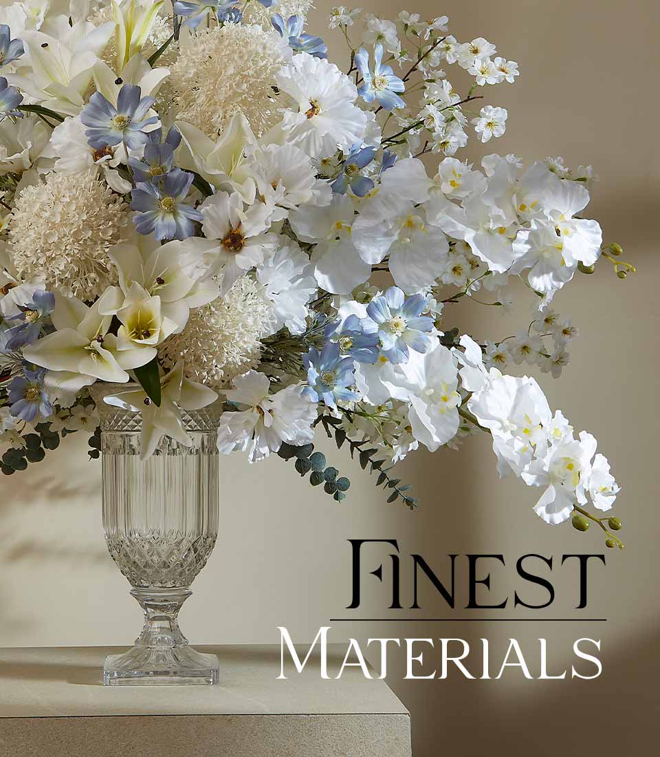 White and light blue artificial orchids, lilies, and eucalyptus in ribbed glass urn vase