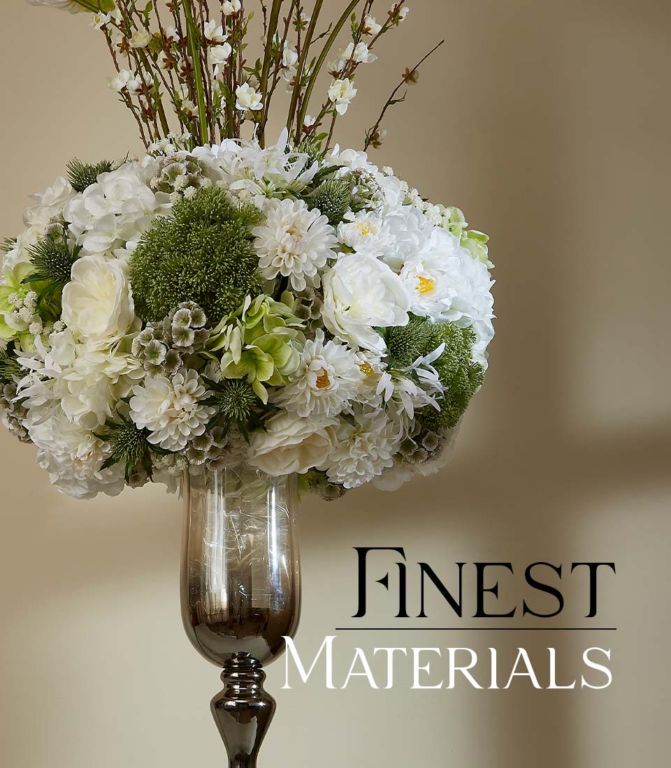 Tall dark glass vase with white hydrangeas, dahlias, and peonies arranged with green thistles and branch accents