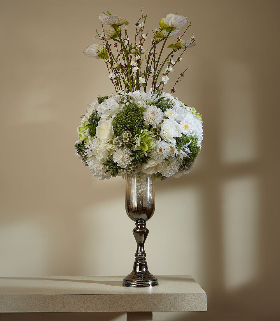 Tall bronze and smoky glass vase with white and blush artificial flowers, spherical arrangement with calla lily stems