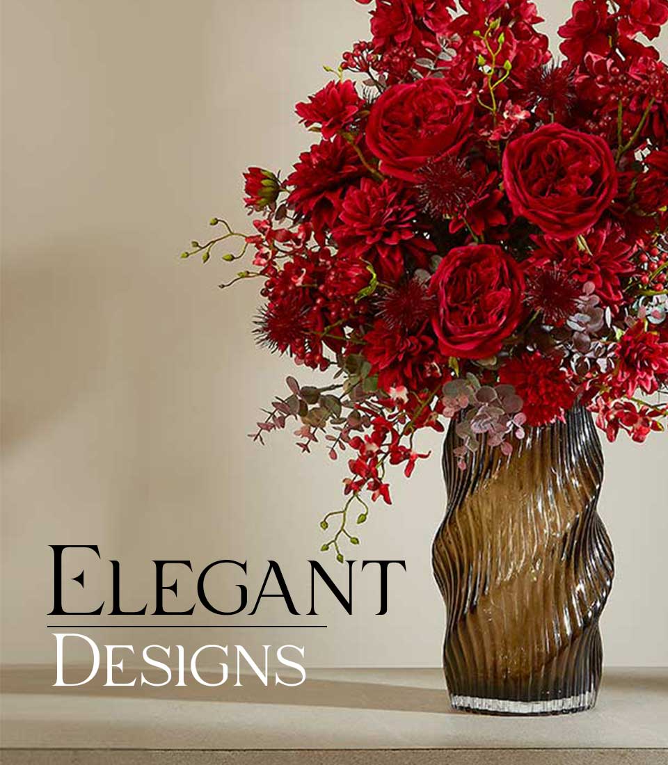 Graceful red luxury artificial flower arrangement in dark amber textured glass vase, featuring full roses and dahlias with