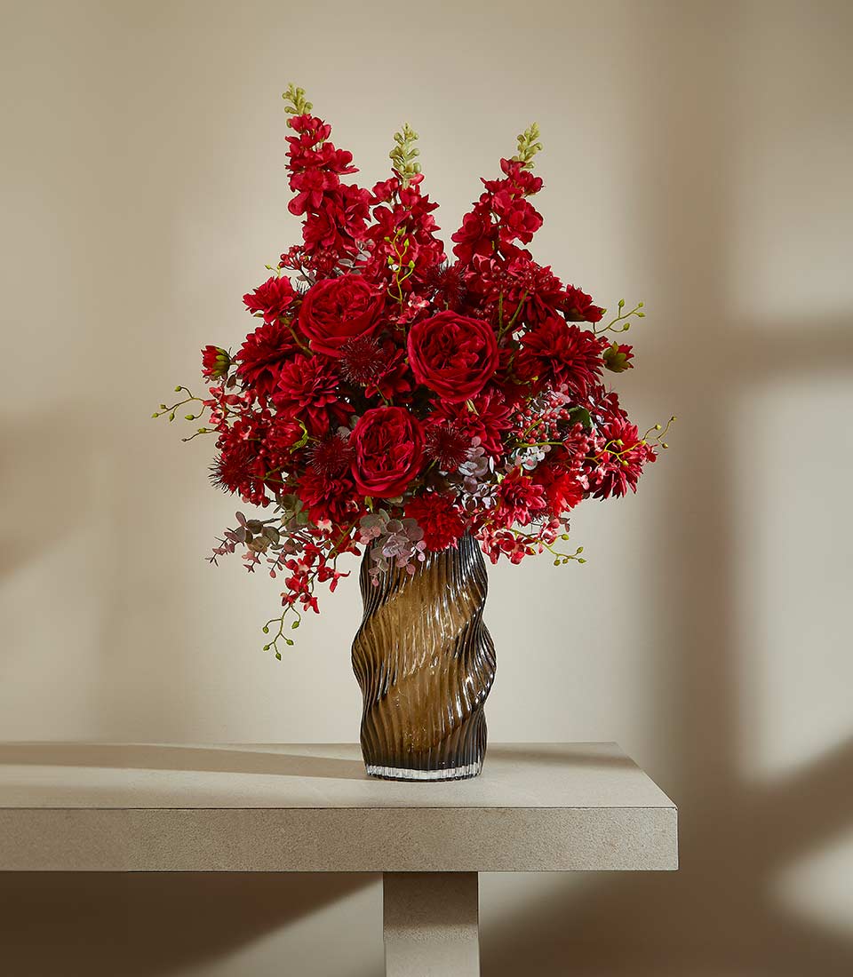 Graceful red luxury artificial flower arrangement in dark textured glass vase with roses and delphinium