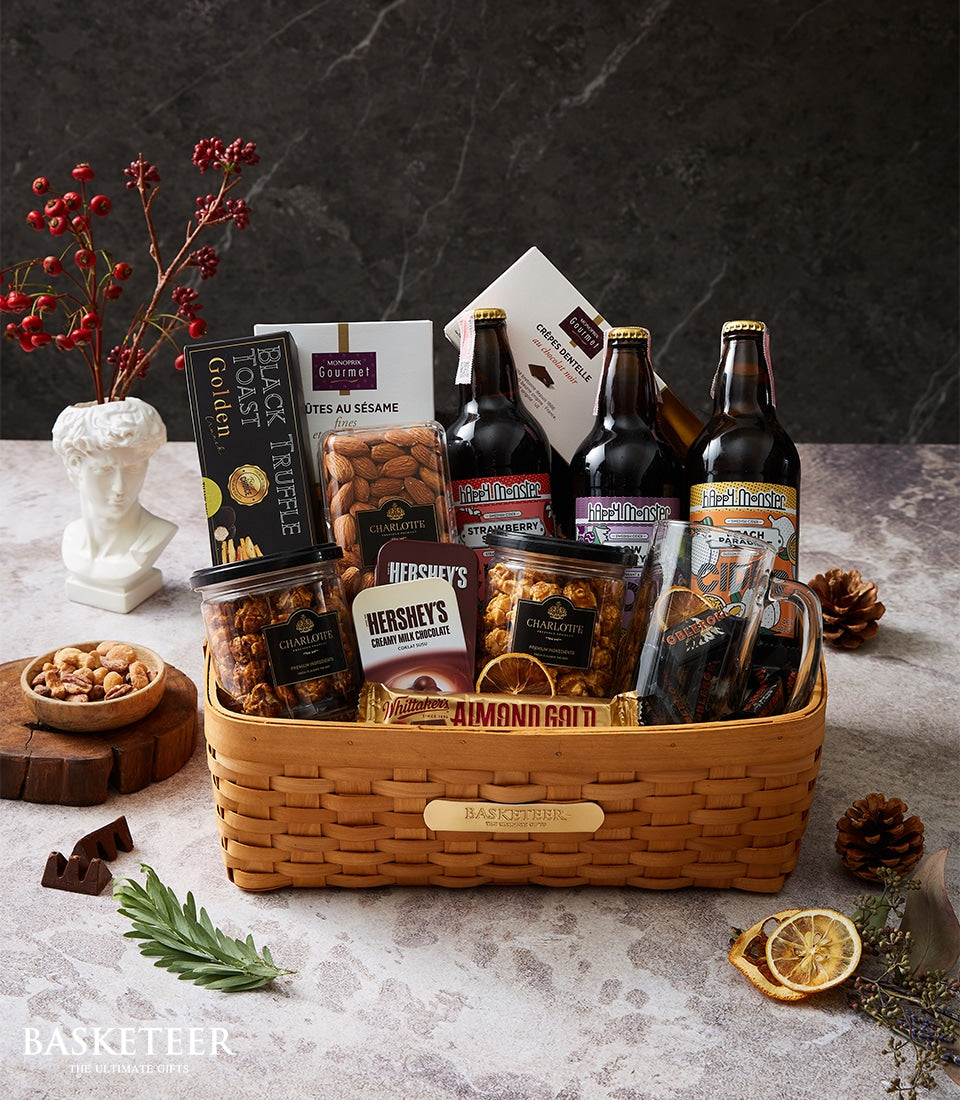 Woven craft beer and gourmet snack gift basket with chocolate, artisan jars, and festive decorative accents