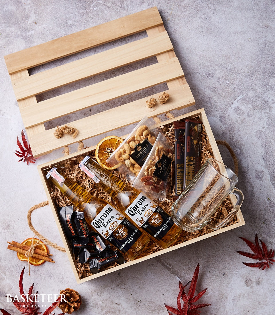 Corona beer gift crate with snacks, chocolates, and glass mug in wooden basket with festive dried fruit garnish