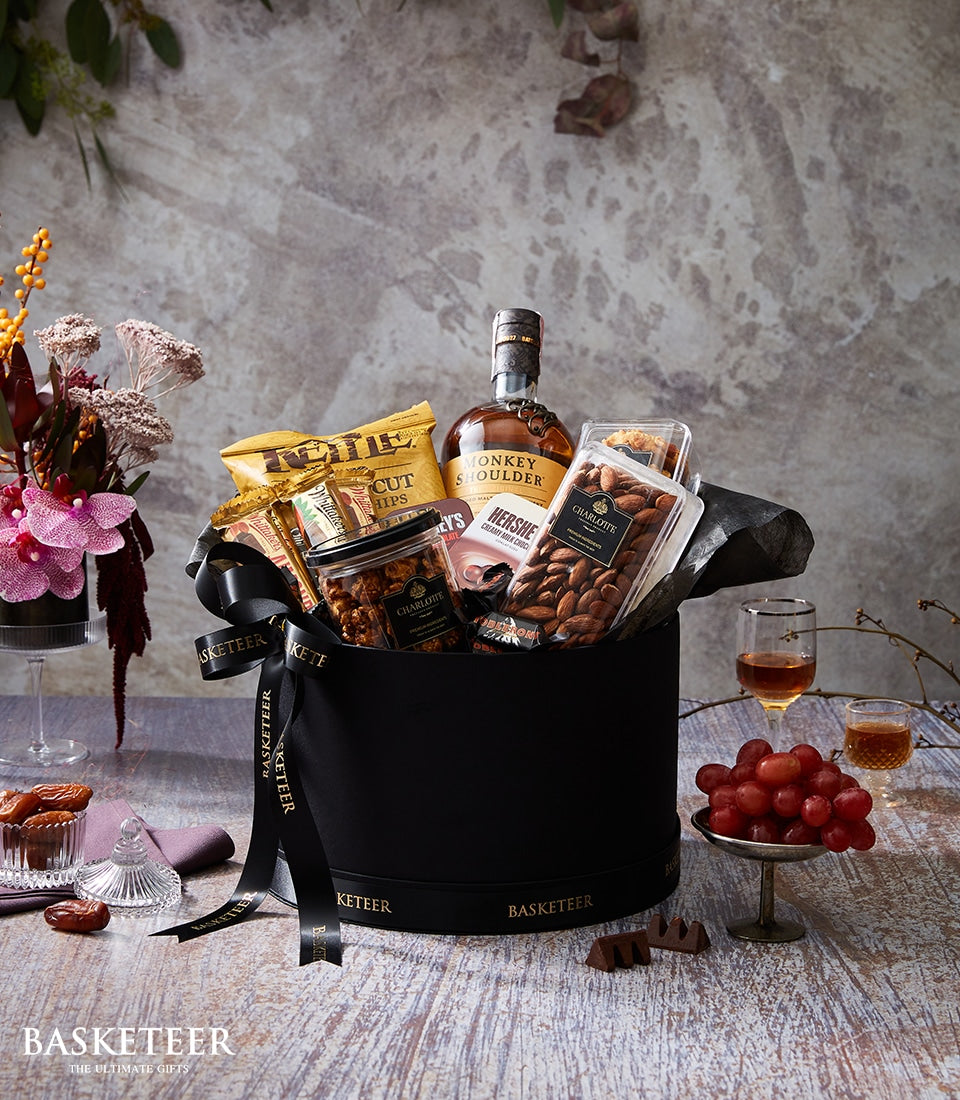 Luxury whisky gift box with chocolate, caramel popcorn, and almonds on rustic wooden table