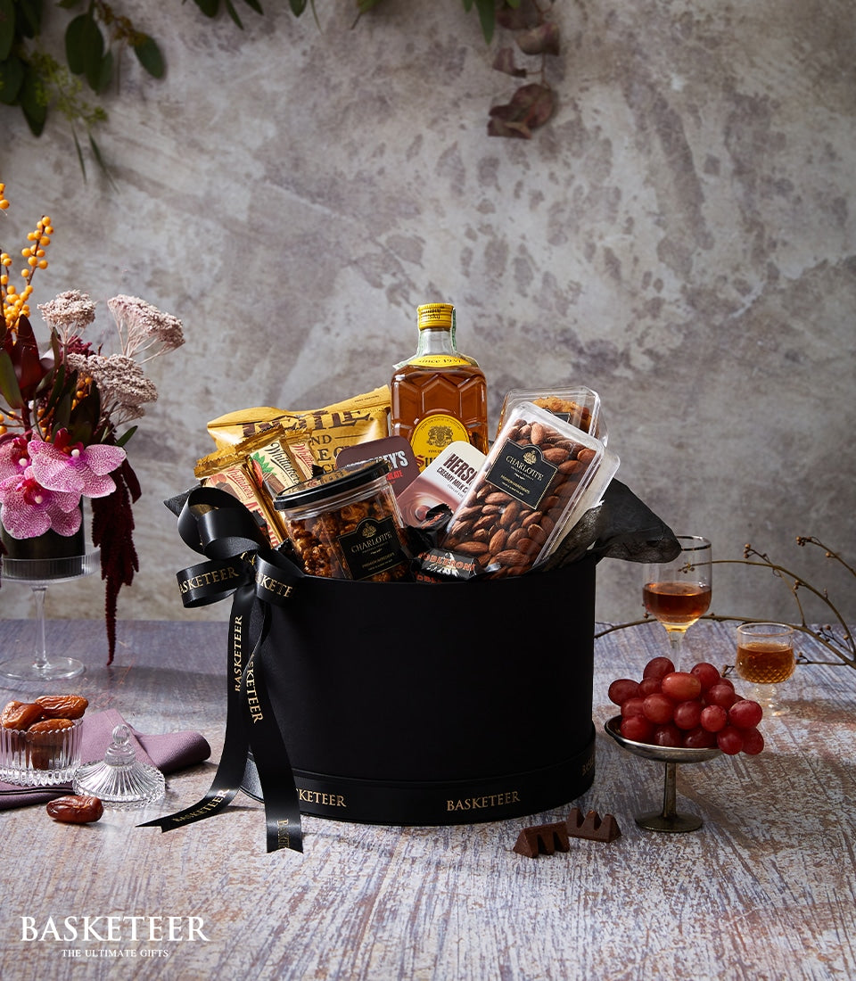 Luxury whiskey gift box with gourmet snacks, chocolates, and nuts on rustic wood with fresh flowers