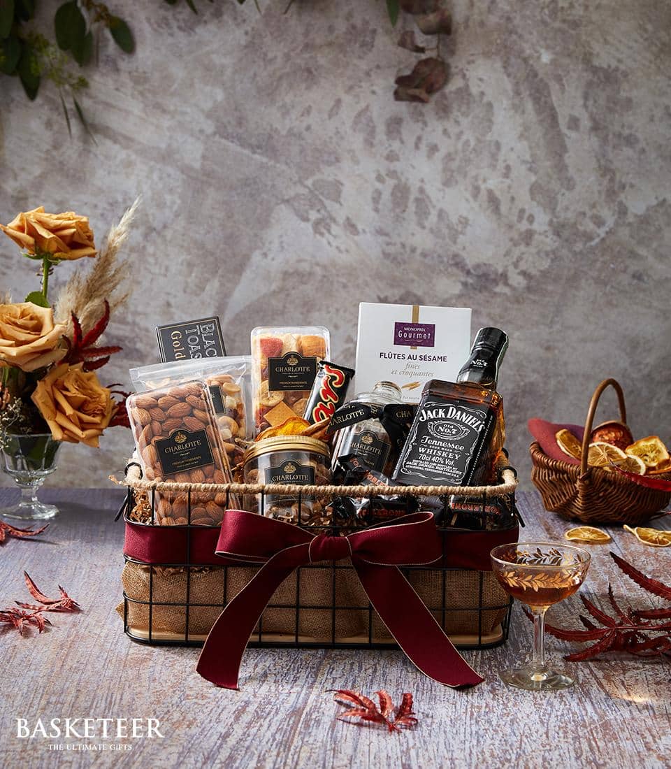 Premium whiskey gift basket with gourmet nuts, crackers, chocolate, and deep red velvet ribbon on dark metal frame