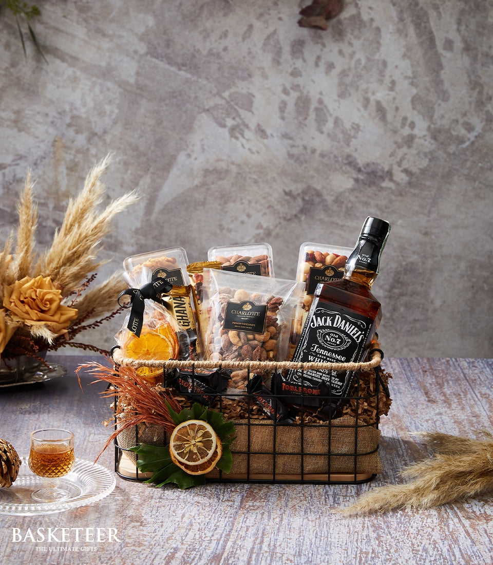 Premium whiskey gift basket with Jack Daniel's, gourmet nuts, chocolate, and dried botanicals in dark wire hamper