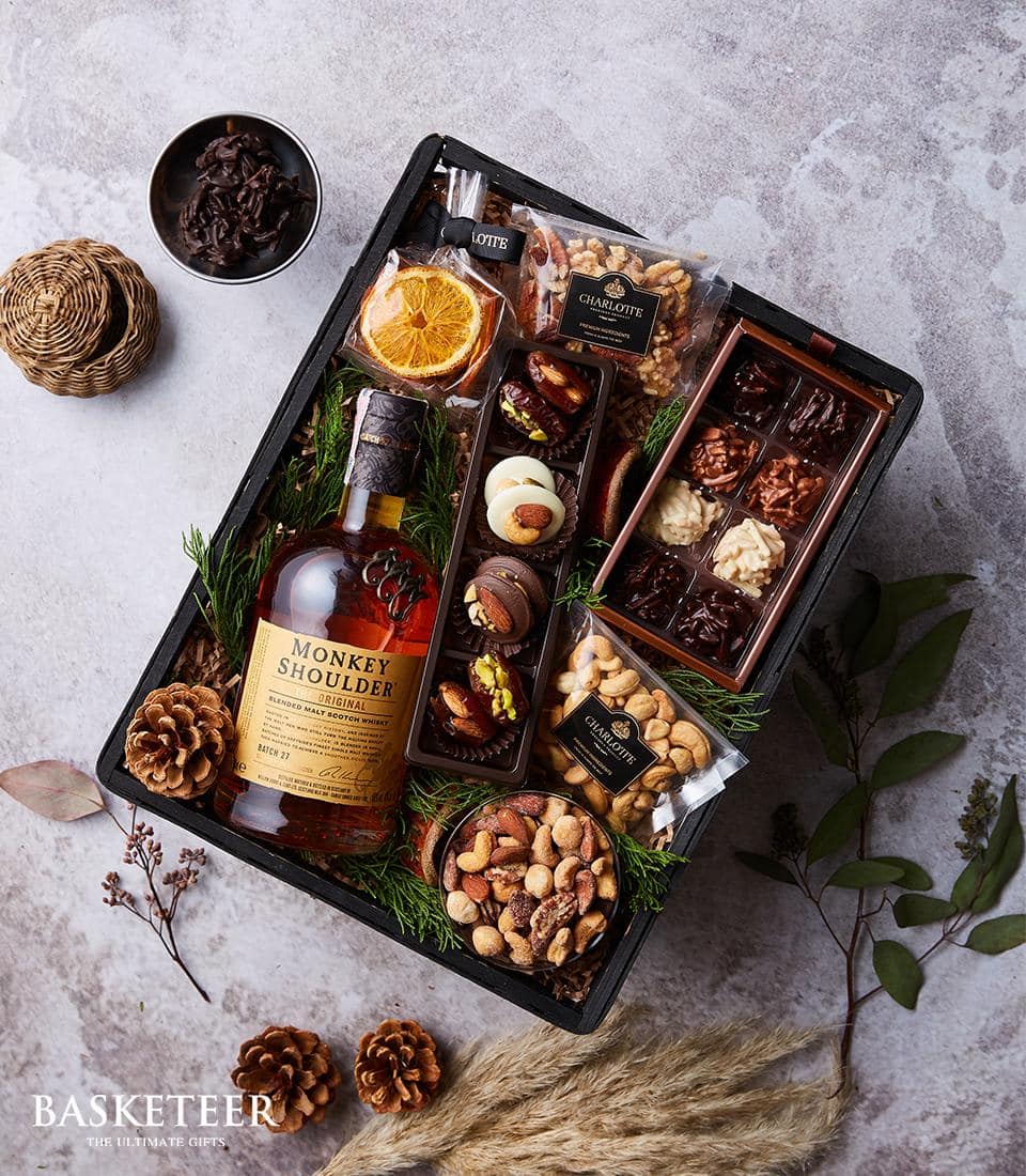 Luxury whisky gift basket with Monkey Shoulder Scotch, gourmet chocolates, nuts, and dried fruits in dark woven basket
