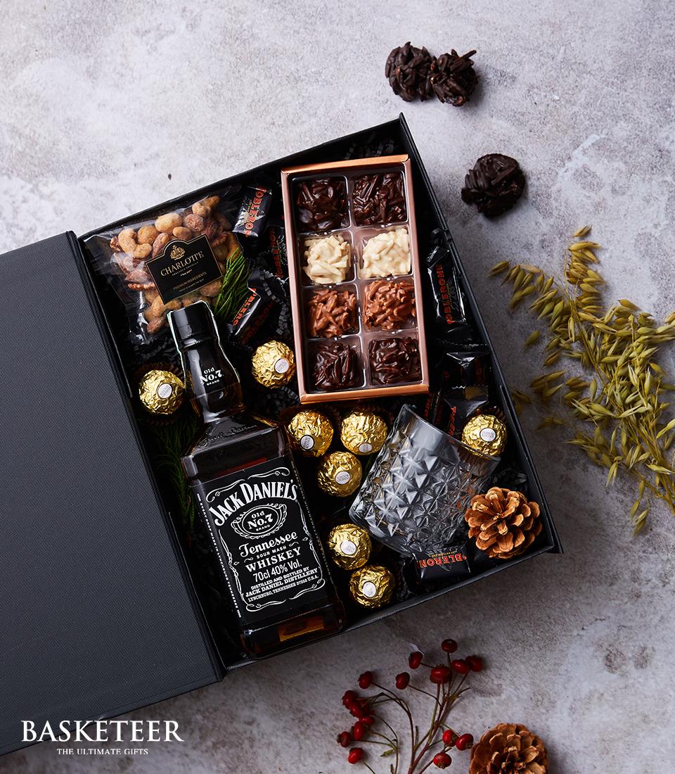 Jack Daniel's whiskey gift box with chocolate, nuts, and faceted glass on grey surface