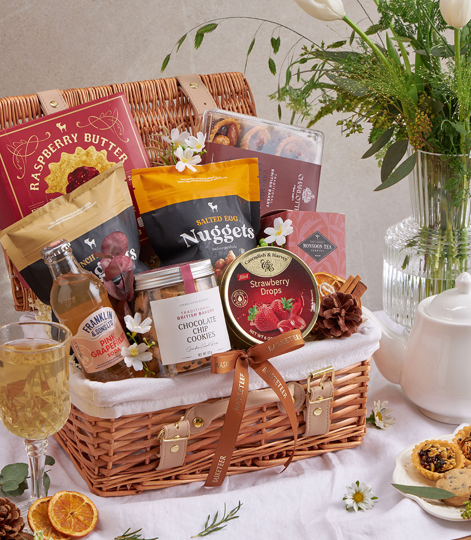Wicker picnic basket filled with gourmet cookies, artisan snacks, premium tea, and dried citrus accents