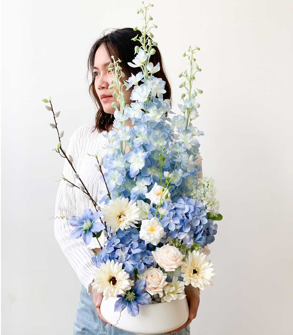 Blue delphinium and hydrangea artificial flower arrangement in white ceramic bowl, perfect for congratulations or gifting