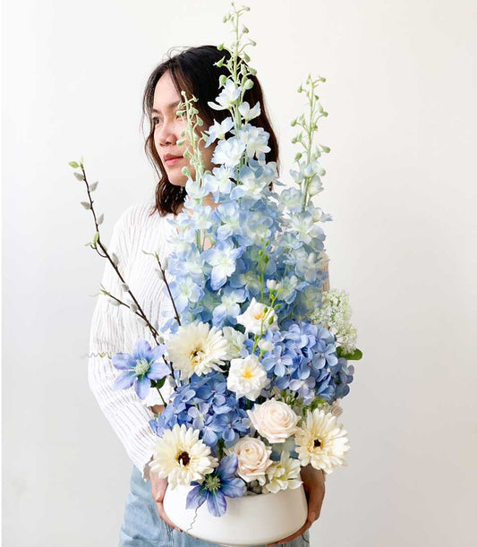 Blue delphinium and hydrangea artificial flower arrangement in white ceramic bowl, perfect for congratulations or gifting
