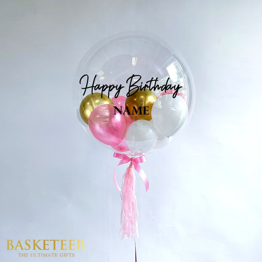 Personalised bubble balloon with gold, pink, and white balloons inside, custom name, pink ribbon and tissue tassels