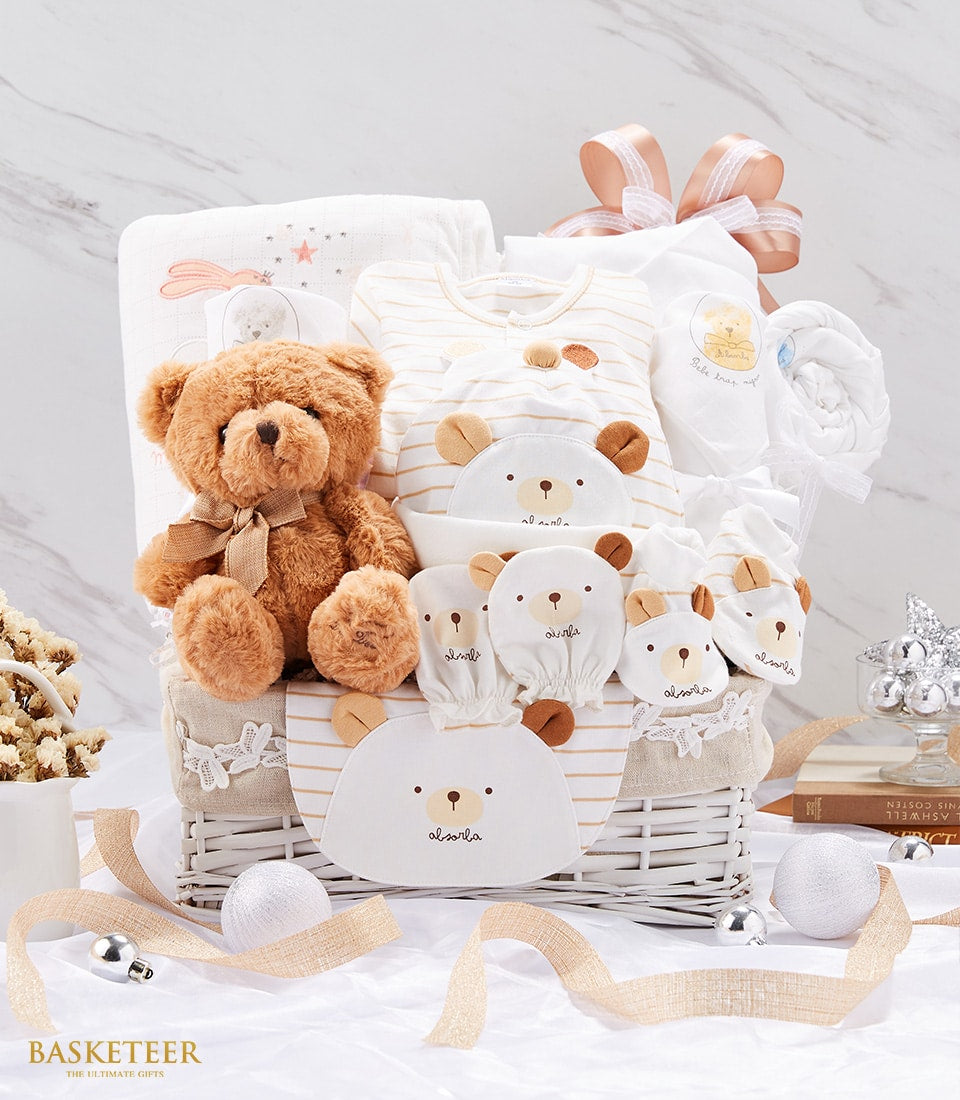 Newborn baby gift basket with brown teddy bear, cream striped onesies, and white woven basket tied with pink ribbon