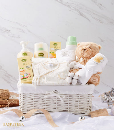 White wicker baby gift basket with teddy bear, onesie, and gentle bath products in soft yellow and green packaging