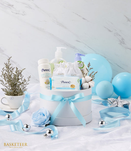 Newborn baby gift set in white round box with light blue ribbon, featuring baby powder, bottles, wipes and pouches