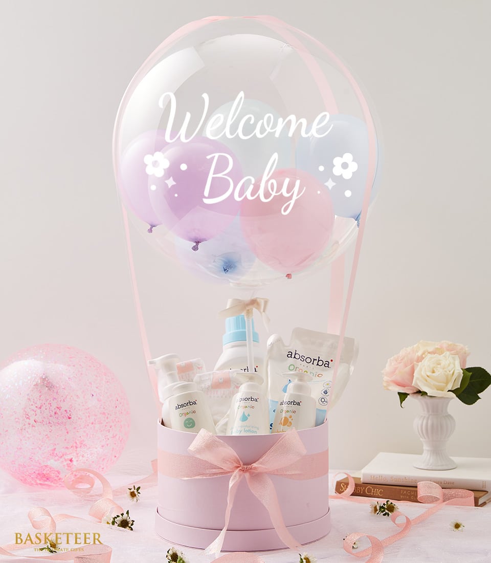Newborn welcome gift set with pastel balloons, pink gift box, organic baby care products, and fresh pink roses