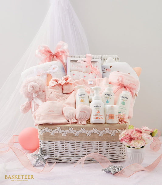 Pink newborn gift basket with organic baby essentials, clothing, teddy bear, and flowers