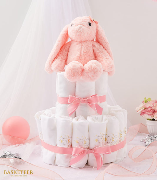Two-tier pink and white diaper cake with plush bunny, gold teddy bear pattern, and fresh pink flowers for newborn