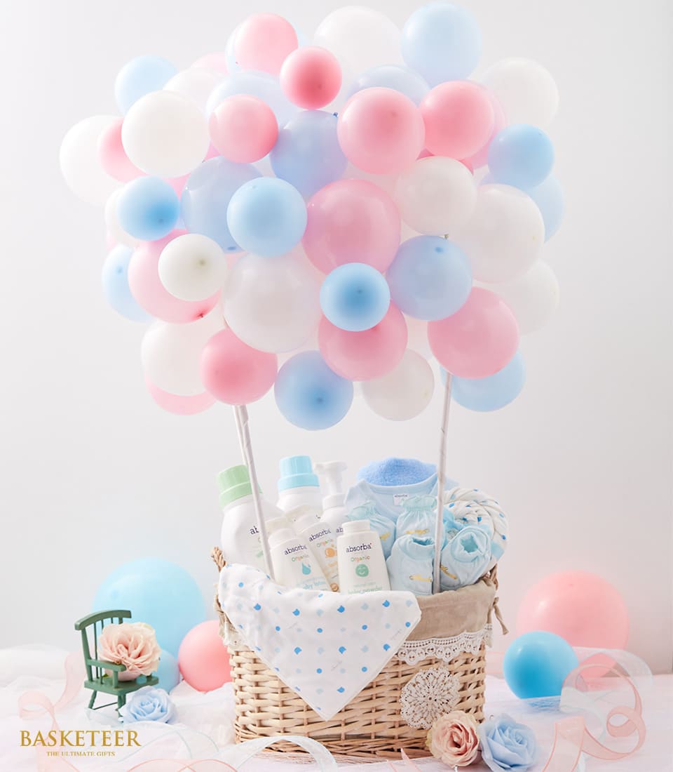 Pastel hot air balloon baby gift basket with wicker base, filled with newborn care essentials and soft blankets