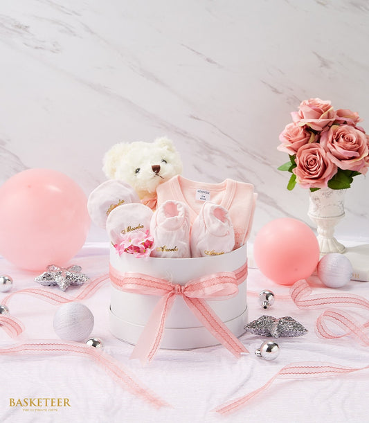 Sweet pink newborn gift set with teddy bear, onesie, and booties in white round box with pink ribbon