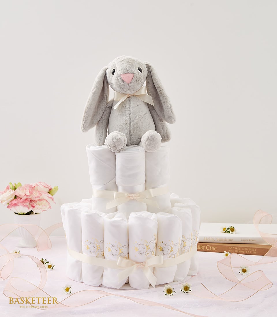 Gray plush bunny with cream bow atop tiered white diaper cake gift set for newborns