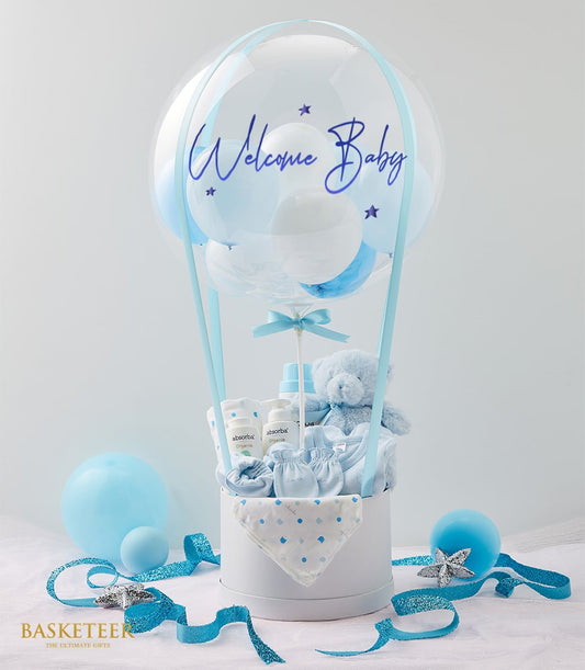 Blue and white hot air balloon baby gift set with plush teddy, organic bottles, and clothing in welcome hamper