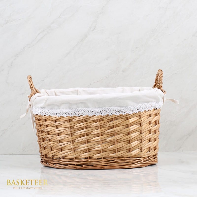 Tall light brown wicker gift basket with white lace-lined interior and braided handles