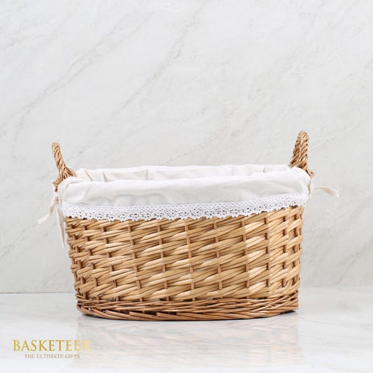 Tall light brown wicker gift basket with white lace-lined interior and braided handles