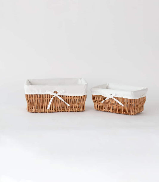Pair of light brown woven wicker storage baskets with white fabric liners and ribbon bows, ideal for luxury gift hampers