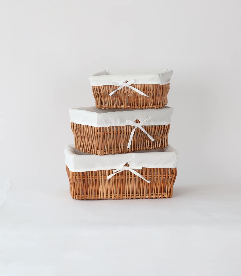 Stacked brown wicker storage baskets with white fabric liners and ribbon bows