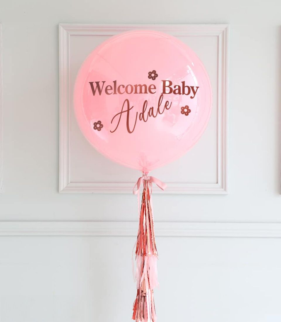 Personalised pink welcome baby balloon with rose gold lettering and decorative tassel garland
