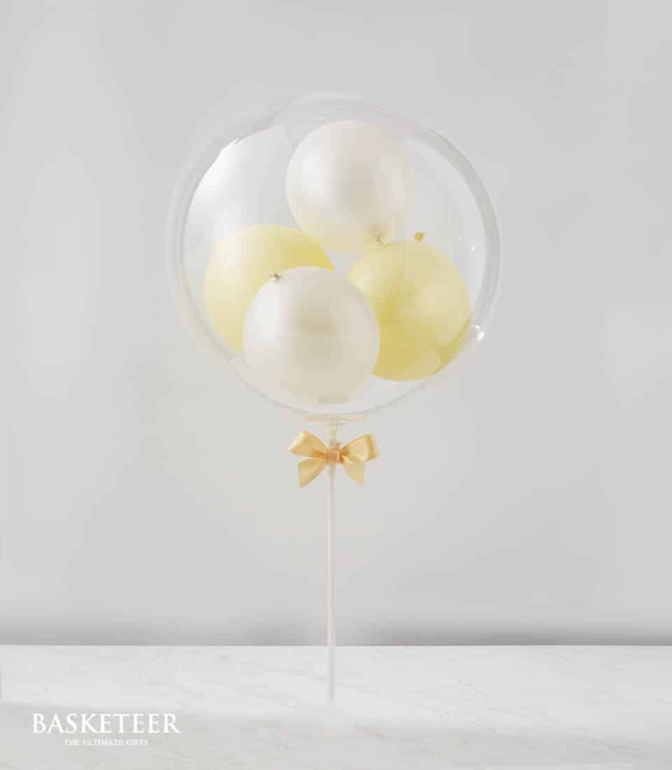 Clear balloon filled with pale yellow and off-white mini balloons, tied with gold satin ribbon
