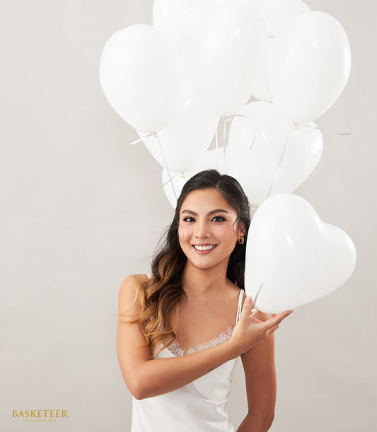 White heart-shaped balloon bouquet with delicate cream tones, held by smiling woman in white satin for romantic gifting
