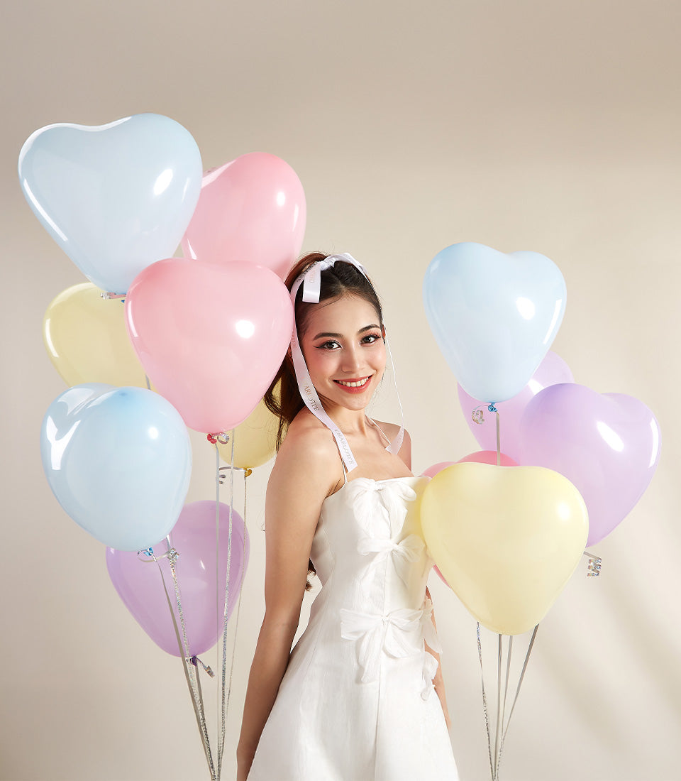 Woman in white dress surrounded by pastel heart-shaped balloons in pink, blue, and lavender for Valentine's Day surprise gift