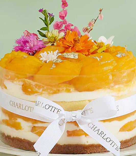 Mango charlotte cake with fresh flowers, layers of mango and cream, silver leaf detail in clear cylinder
