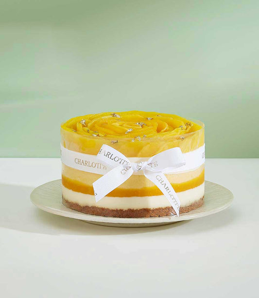 Exotic mango layer cake with creamy white mousse, mango spiral topping, and gold leaf detail, tied with Charlotte ribbon
