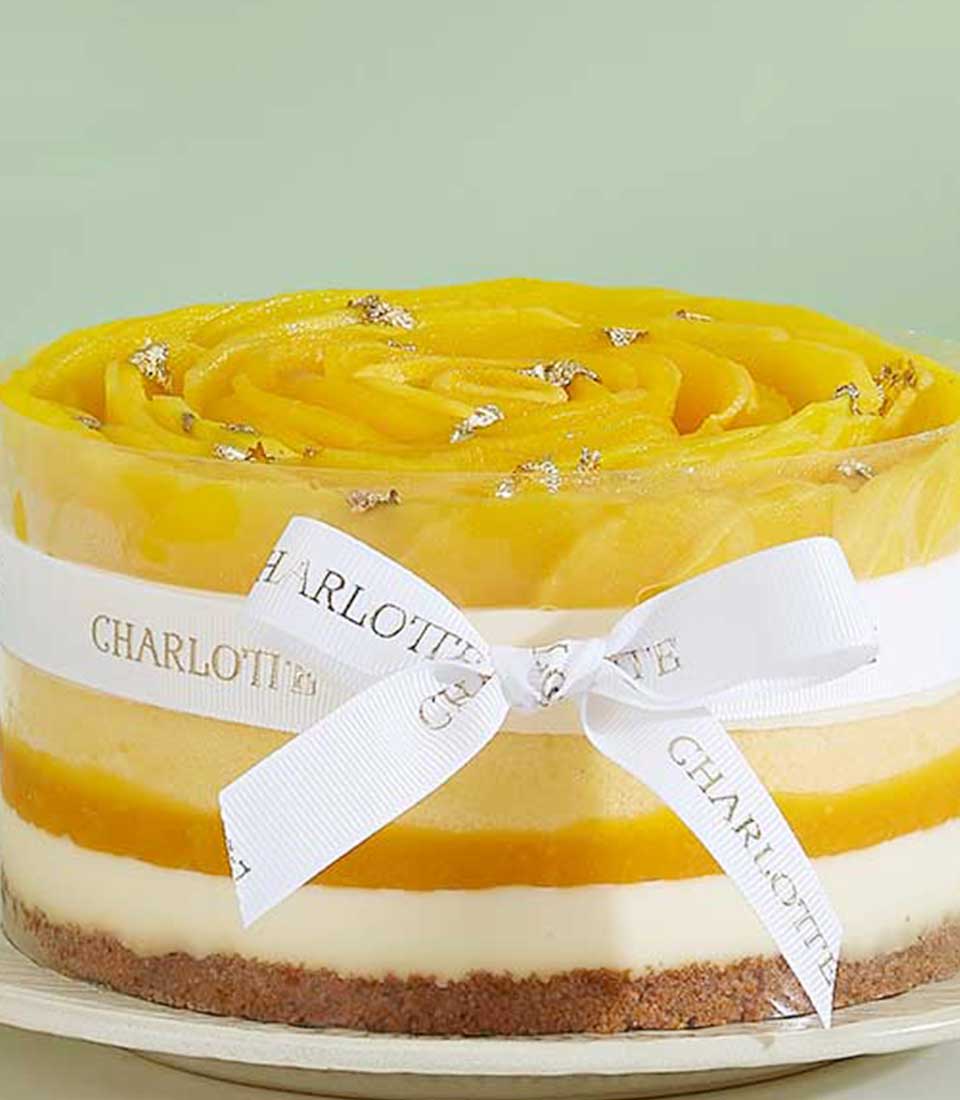 Exotic mango layer cake with creamy white mousse, dark crust, and golden mango rosette topped with edible glitter